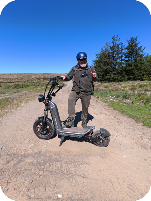 A smiling man wearing a helmet and outdoor gear poses on a dirt path with his F7ULTRA electric scooter.