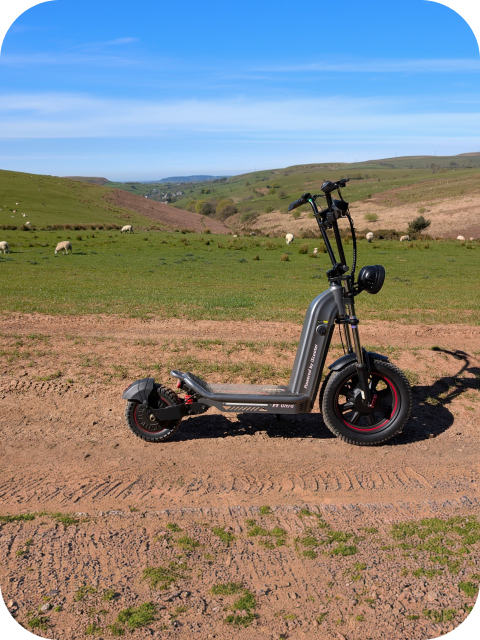 The F7ULTRA electric scooter sits on a dirt path set against a scenic, hilly landscape featuring grazing sheep under a clear blue sky.