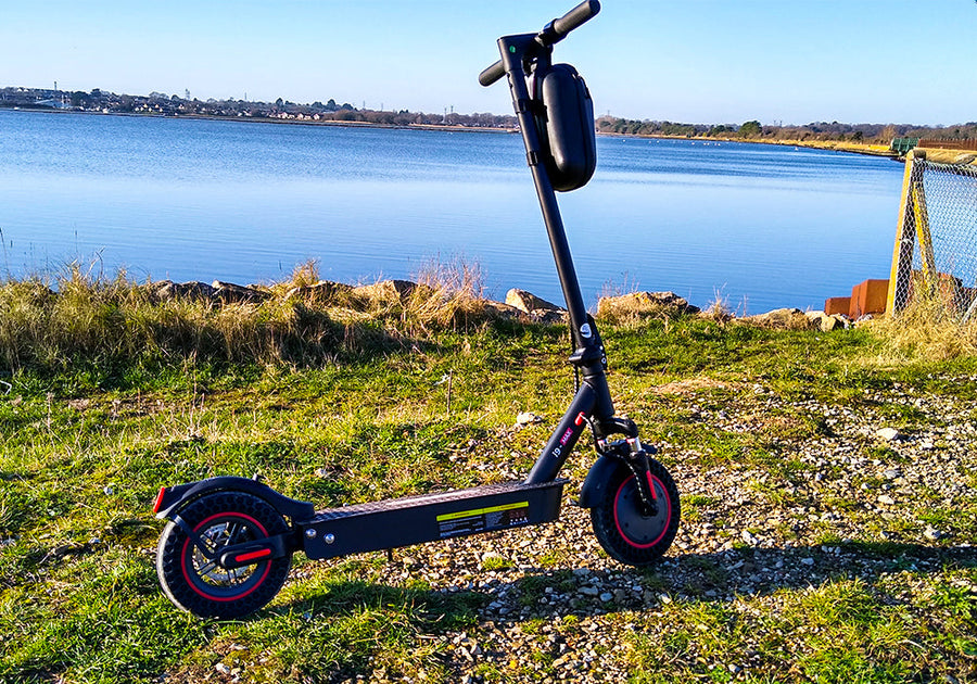 iScooter i9 Max electric scooter with a bright front headlight, rear brake light, foldable design, and a smartphone displaying the companion app interface for monitoring ride data and adjusting scooter settings.