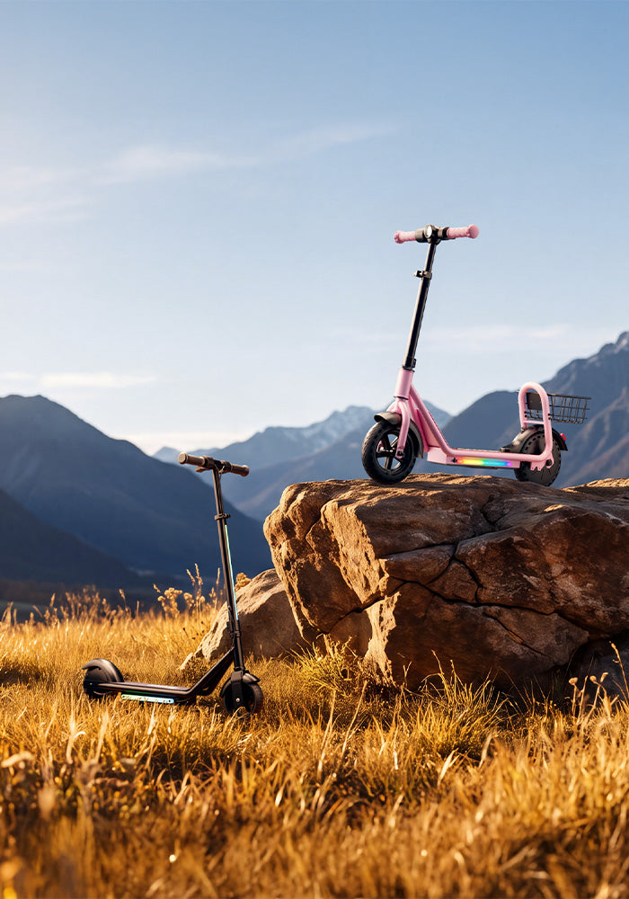 Vertical photo of a pink kids' electric scooter with LED lights perched on a rock and a black scooter in a grassy field.