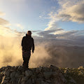 Silhouette of a person standing on a hill against a cloudy sunset sky.