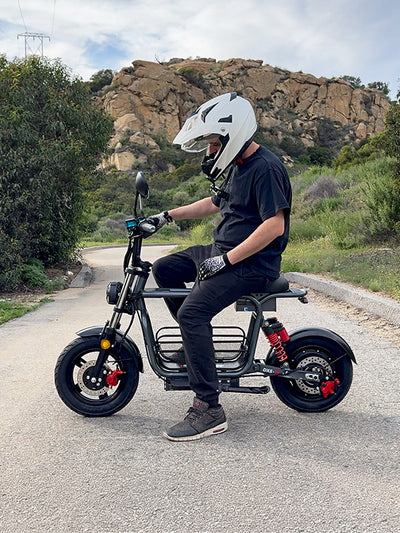 A person wearing a helmet sitting on a black iScooter DX5 electric bike outdoors.