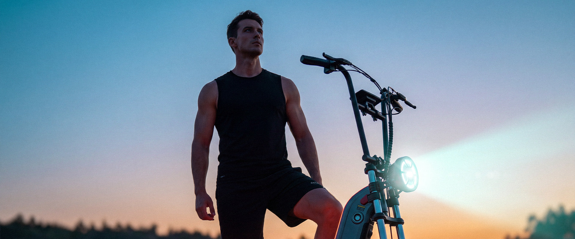 Rider standing beside the F7 Ultra all-terrain electric scooter at sunset, highlighting its long-range capability of up to 62 miles, powerful performance, and bright front headlight for extended outdoor rides.