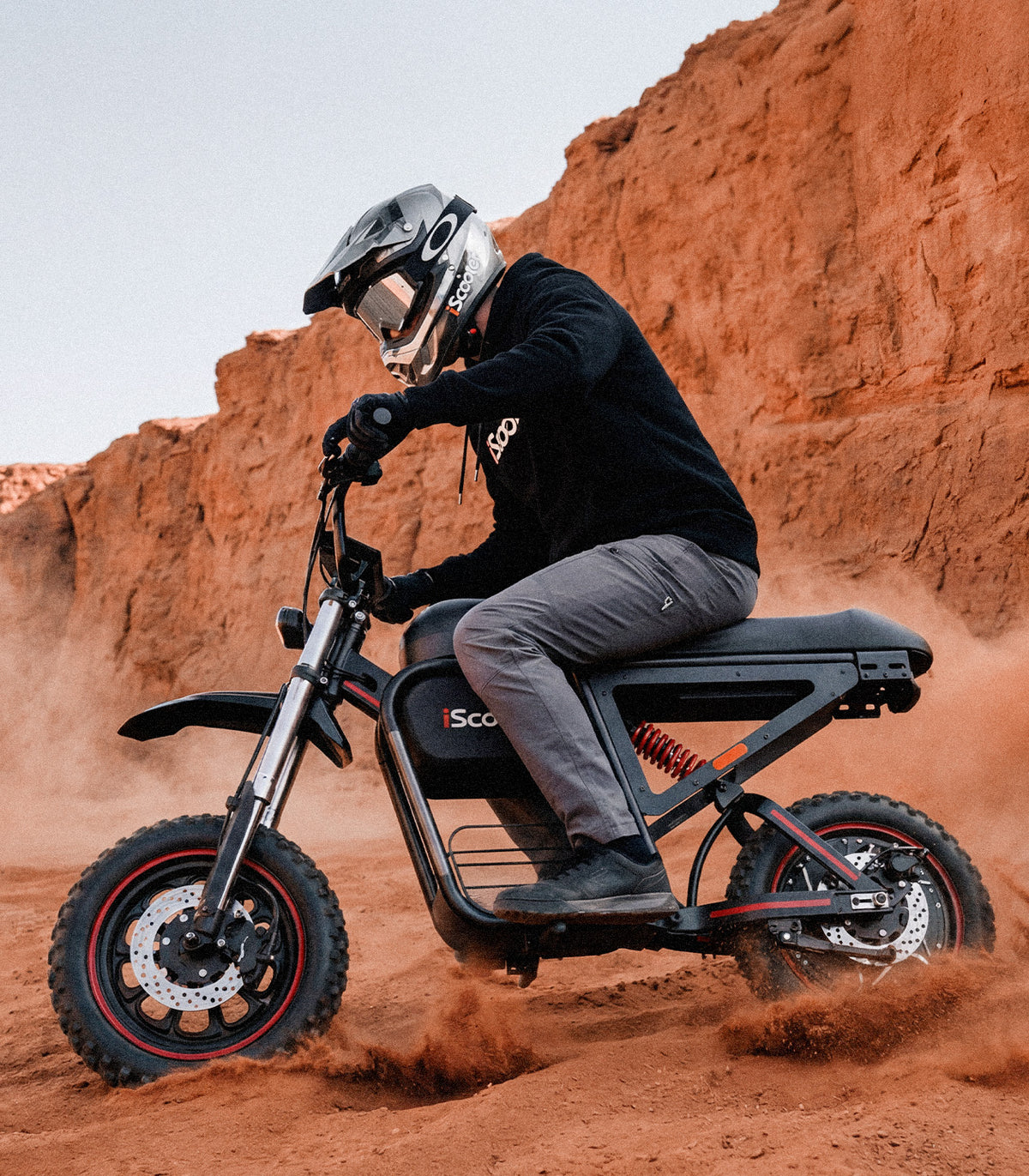 Action shot of a rider on an iScooter DX5 Max electric bike navigating sandy desert terrain. The bike’s large front and rear disc brakes are clearly visible as sand sprays around the tires, highlighting braking performance, control, and stability in challenging off-road conditions. The rocky canyon backdrop reinforces the bike’s rugged adventure capability.