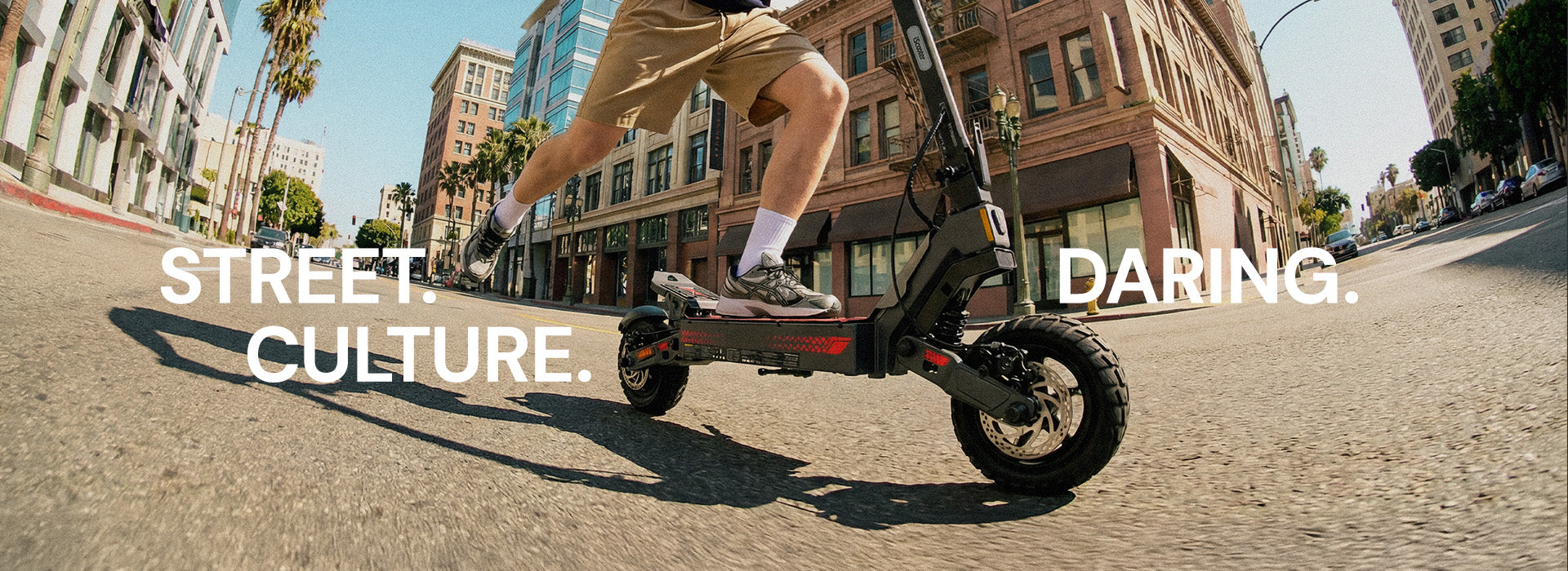 Person riding an iScooter iF1 electric scooter through a city street, captured from a low-angle action shot with urban buildings in the background, highlighting street culture and dynamic commuting.
