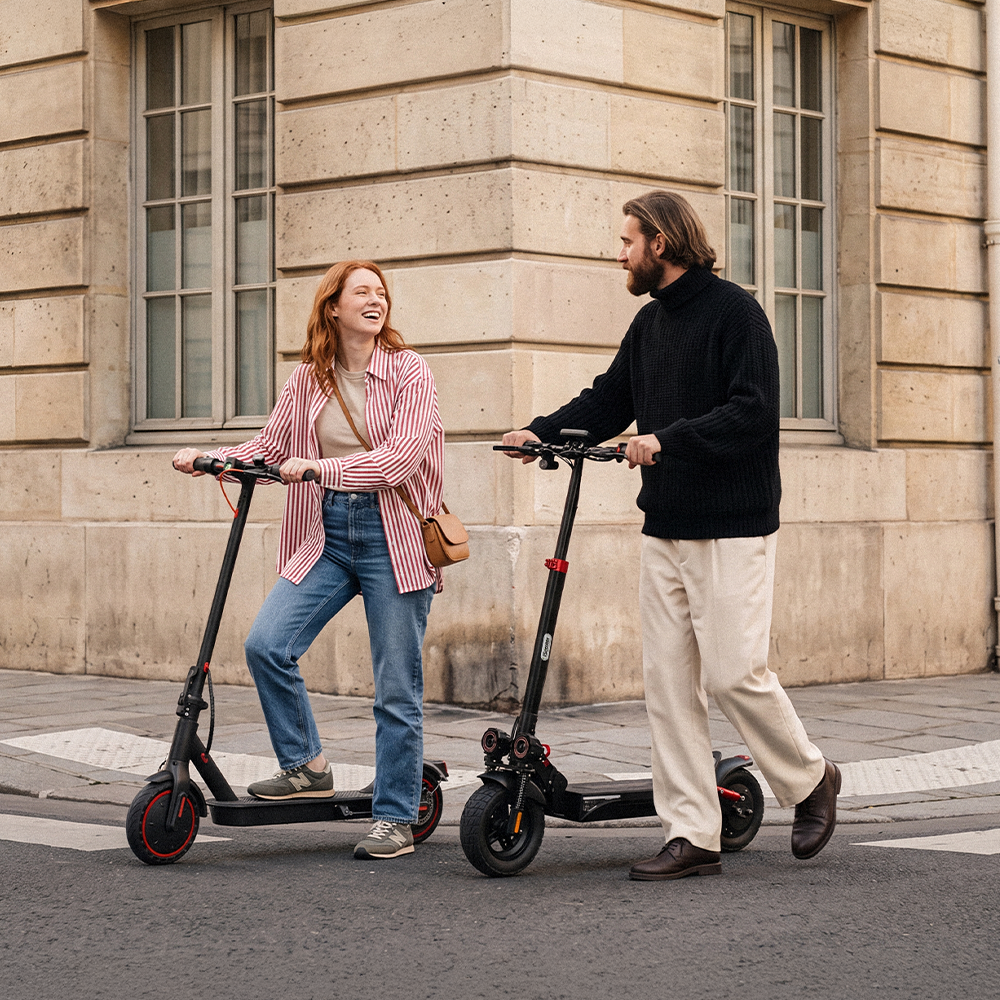Two friends smiling and chatting while walking with electric scooters along a city street lined with historic buildings. The relaxed urban scene highlights shared rides, community, and the iScooter affiliate program experience.