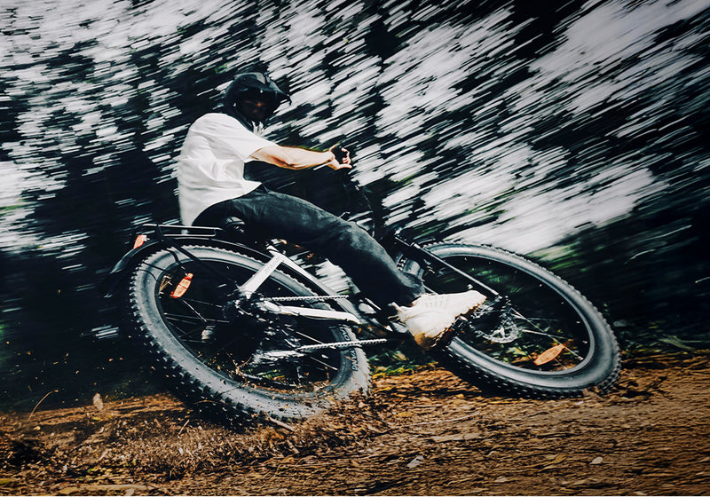 Cyclist leaning into a sharp turn on a dirt path with a motion-blurred background.