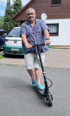 Man riding a scooter on a street with a Volkswagen vehicle in the background