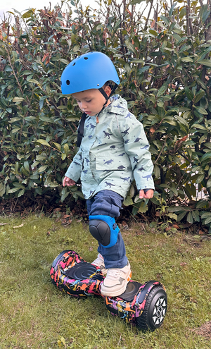 Child wearing a helmet and riding a hoverboard on grass with bushes in the background