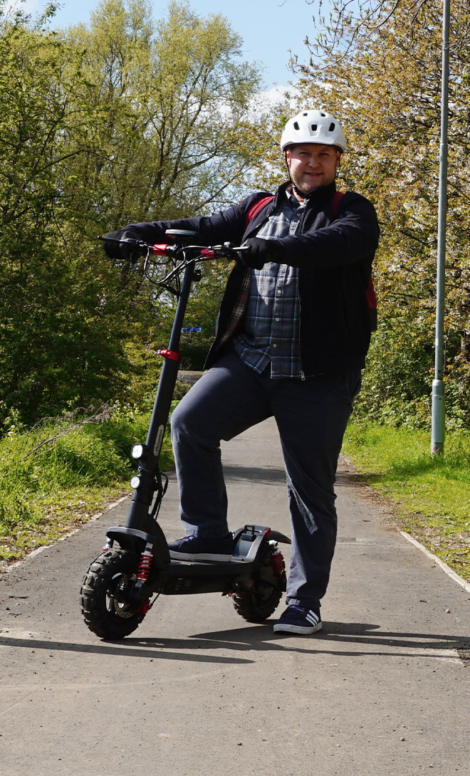 Person riding an electric scooter on a path with trees in the background