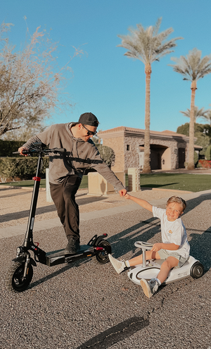 Man with a scooter and child on a toy car in a park setting