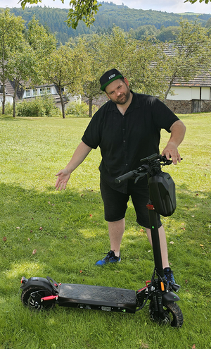Man standing on a grassy area with an electric scooter