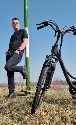 Man leaning against a green post with an electric bike in a field