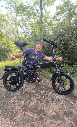 Man posing with an electric bike in a forested area