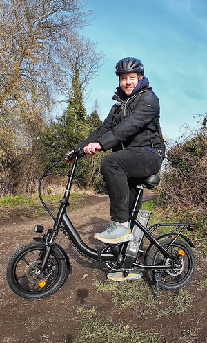 Person riding a black electric bike on a path with trees and blue sky in the background