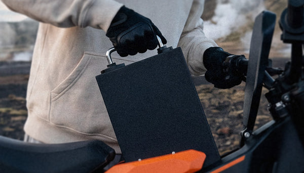 Close-up of a rider removing the detachable battery from the iScooter MT2 electric dirt bike, showcasing the easy-access removable battery system for convenient charging and uninterrupted off-road adventures.