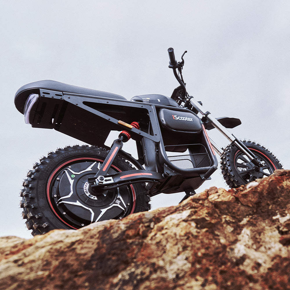 The iScooter DX5 Max electric bike parked on rocky terrain, showcasing its rugged frame, rear suspension, fat off-road tires, and adventure-ready design.