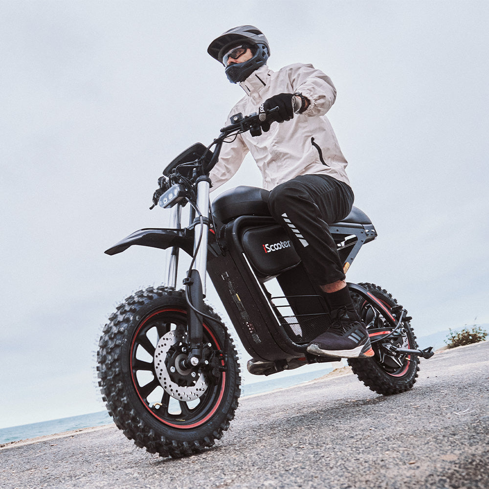 Rider cruising on the iScooter DX5 Max electric bike along a coastal road, highlighting its fat tires, comfortable riding position, and rugged all-terrain design.