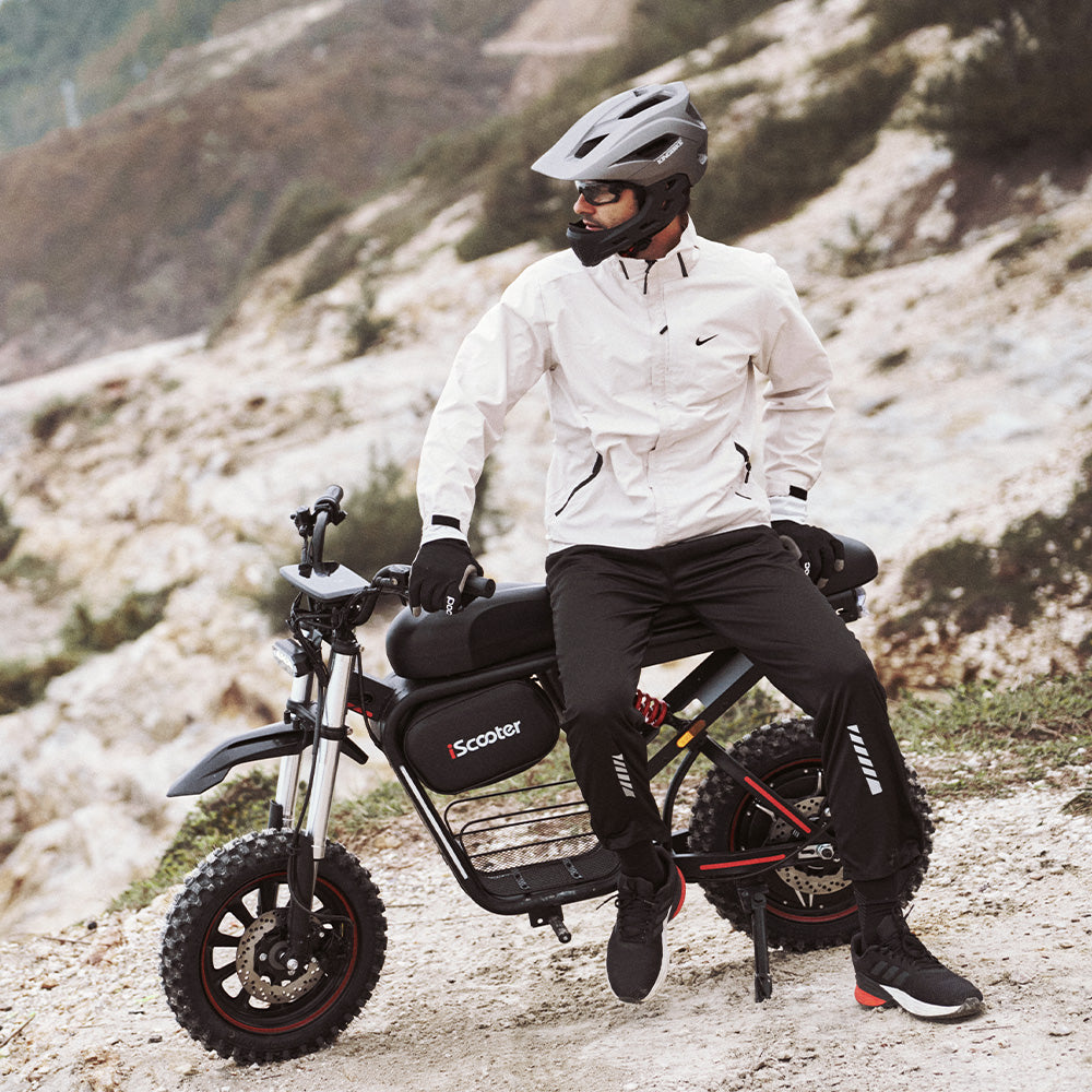 Rider resting on the iScooter DX5 Max electric bike in a rugged outdoor landscape, showcasing its comfortable seat, fat tires, and adventure-ready all-terrain design.