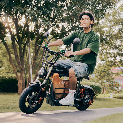 A smiling young man in casual attire and a helmet rides his DX5 electric scooter along a scenic, tree-lined path, carrying a paper bag with a baguette.