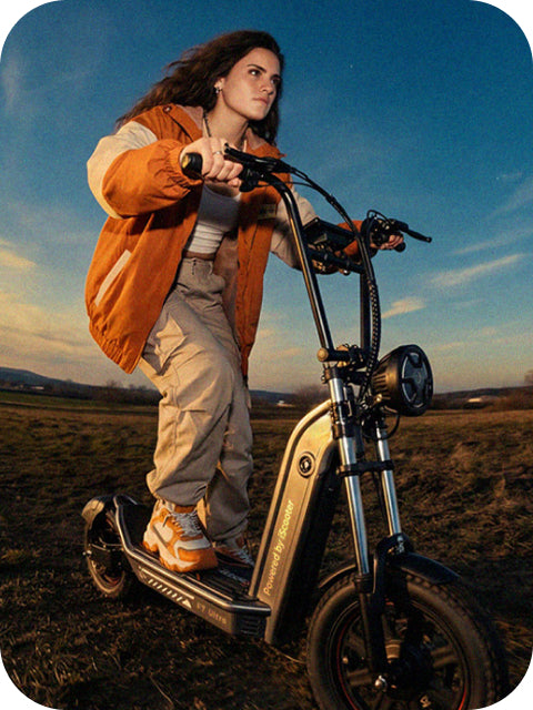A lifestyle photo of a young woman wearing an orange jacket, focused on riding an iScooter F7 Ultra electric scooter across an open, grassy field under a twilight sky.