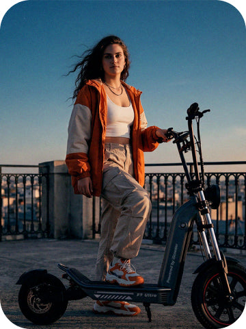 A lifestyle photo of a young woman in an orange jacket standing on the deck of an iScooter F7 Ultra electric scooter outdoors against a evening sky background.