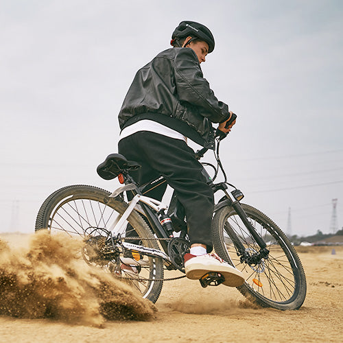 Person wearing a helmet riding an M50 electric bike on sandy terrain, kicking up dust while turning outdoors.