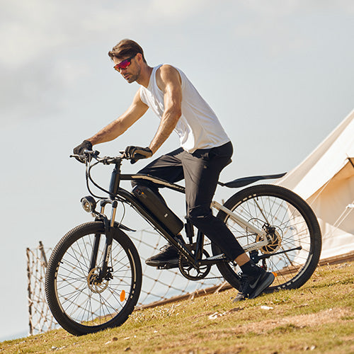 Person wearing sunglasses riding a black M50 electric bike on a grassy hill with tents in the background.