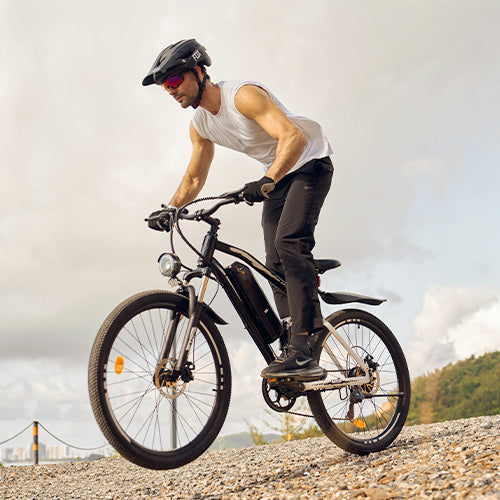 Person wearing a helmet and sunglasses riding a black electric bike on a rocky outdoor trail under a cloudy sky.