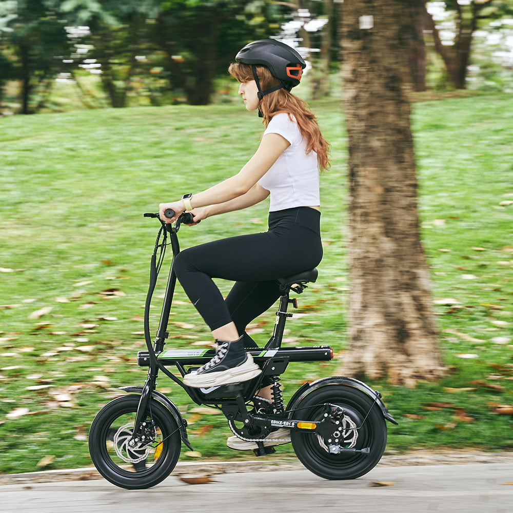Side view of a woman in a helmet riding a compact black EB1S electric bike through a lush park, highlighting its portable design for urban commuting.