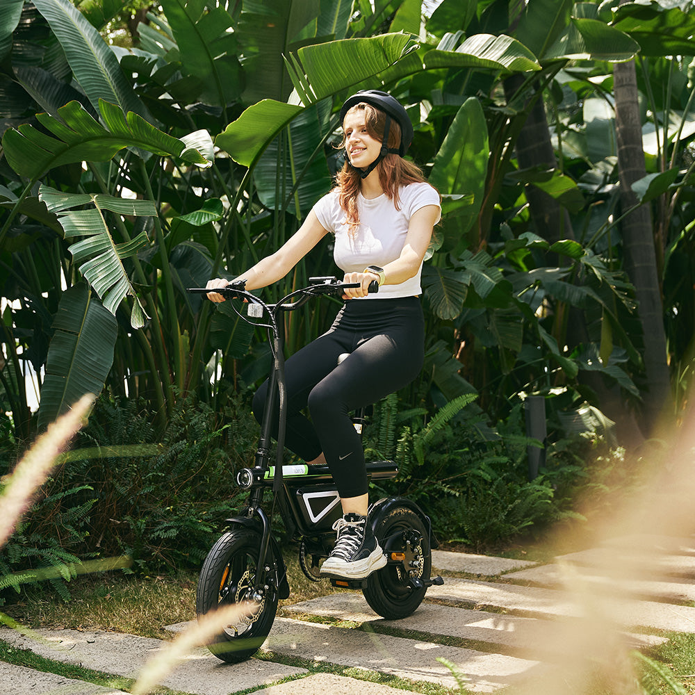 A woman sitting on the ergonomic seat of a compact EB1S electric bike, showcasing its rear suspension and sturdy frame in a bright, outdoor tropical setting in UK.