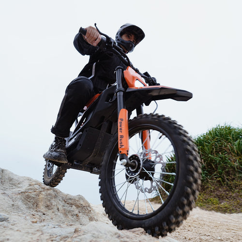 Rider wearing a full-face helmet and protective gear seated on an orange and black MT2 electric dirt bike on a sandy trail, showcasing the bike's off-road stance and rugged design.