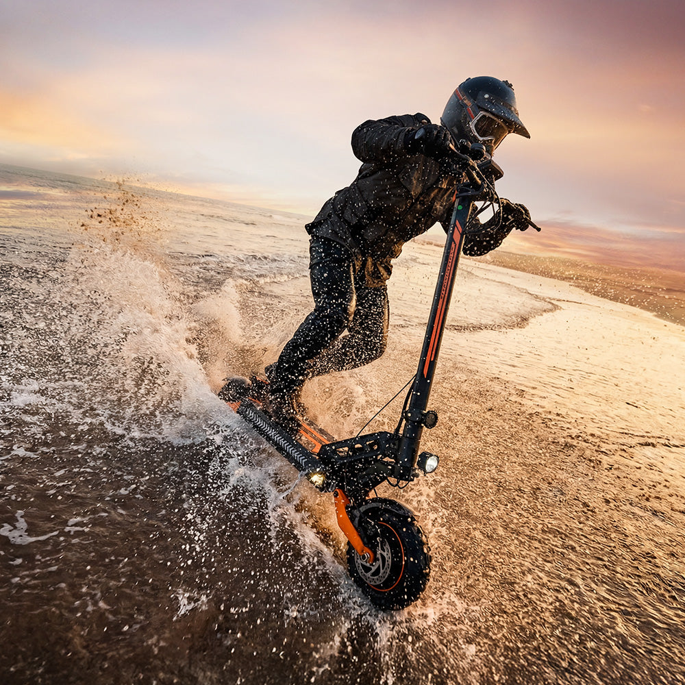 Side view of a foldable black electric scooter with orange accents, shown in its folded position with off-road tires, front suspension, disc brakes, and kickstand against a white background.