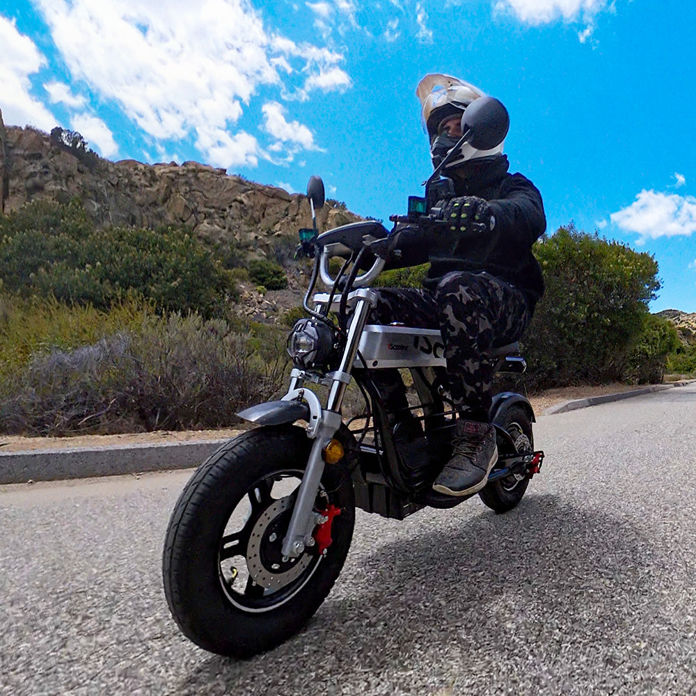 A rider wearing a helmet riding an iScooter DX5 Pro electric scooter on a paved road.
