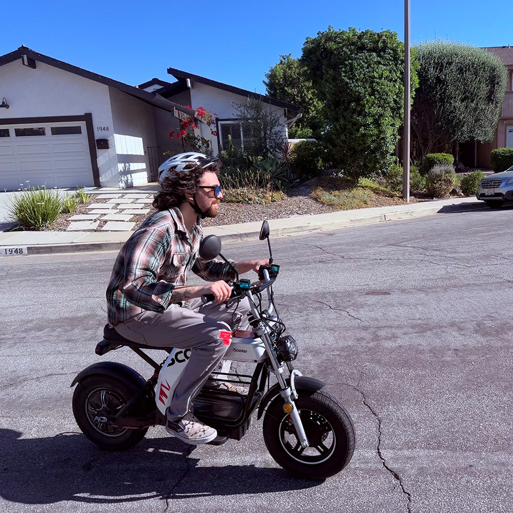 A person riding an iScooter DX5 Pro electric motorbike down a residential street.