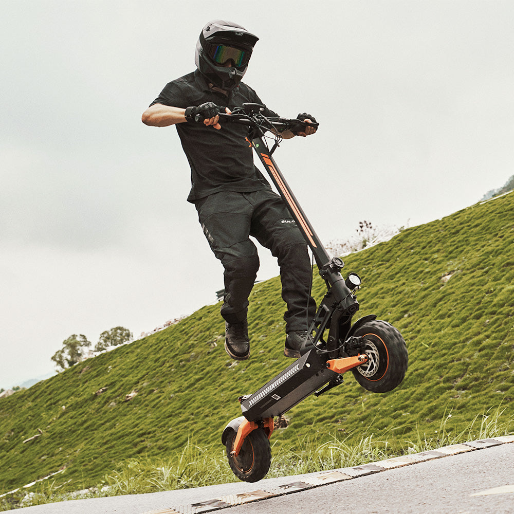 A rider in full gear performing a jump on an off-road electric scooter on a grassy hill.