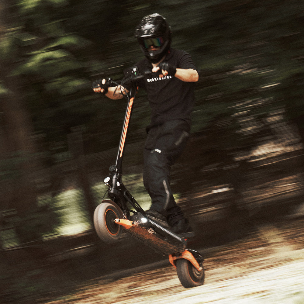 A rider in full gear performing a wheelie on an off-road electric scooter in motion.