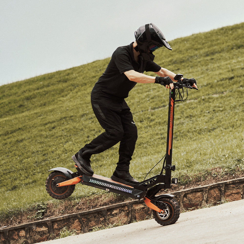A rider in full gear performing a stoppie on an off-road electric scooter on a grassy hill.