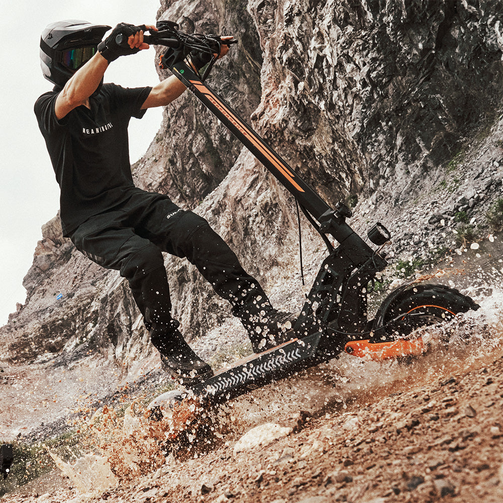 A rider in full gear splashing through water on an off-road electric scooter.