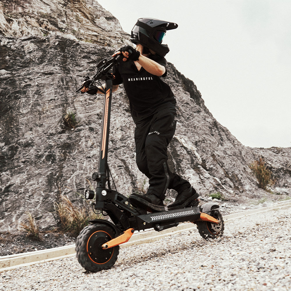 A rider in full gear riding an off-road electric scooter on a rocky dirt path.