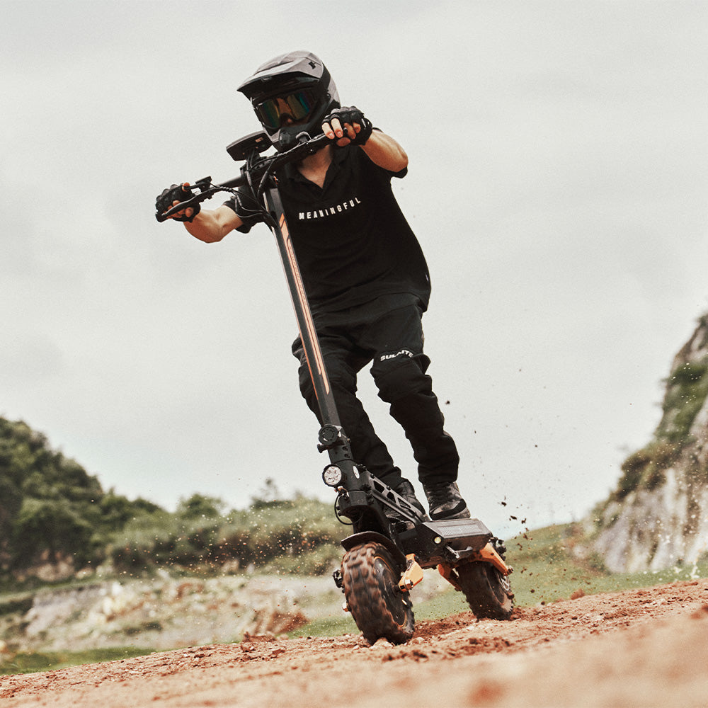 A rider in full gear kicking up dirt while riding an off-road electric scooter on a trail.
