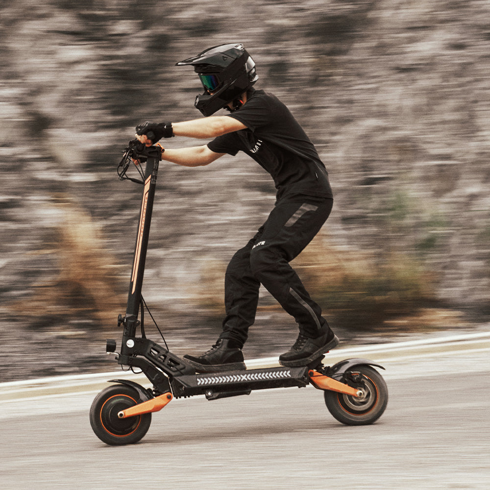 A rider in full gear leaning forward while riding an off-road electric scooter on a paved road.