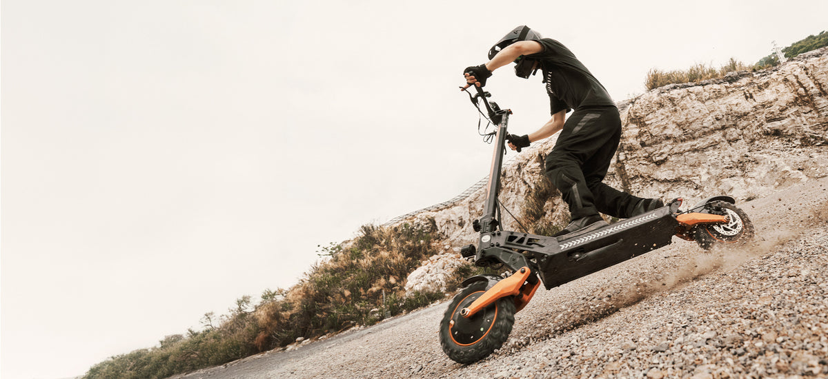 A rider in full protective gear riding an off-road electric scooter down a rocky incline.